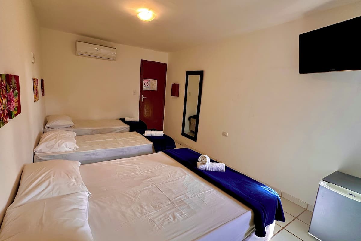 Habitación de hotel con tres camas, un televisor, un espejo y una puerta roja.
