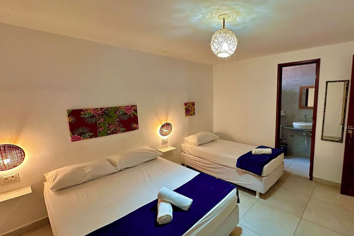 Habitación de hotel con dos camas, baño con lavamanos y una lámpara decorativa en el techo.