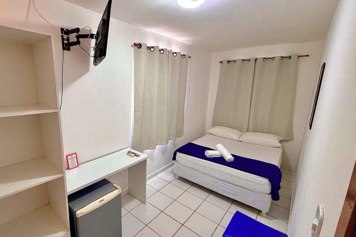 Habitación de hotel con cama, escritorio, silla, televisor montado en la pared y baño con cortina de ducha.