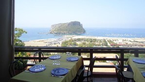 A dining area with tables set for two, overlooking a coastal landscape with a prominent rock formation and beach. - Hotel i Normanni (Praia a Mare)