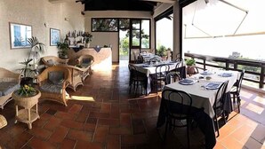 A dining area with wicker furniture, a table set for two, and a view of the outdoors. - Hotel i Normanni (Praia a Mare)