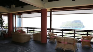 A spacious indoor area with wicker furniture, large windows, and a view of a mountainous landscape. - Hotel i Normanni (Praia a Mare)