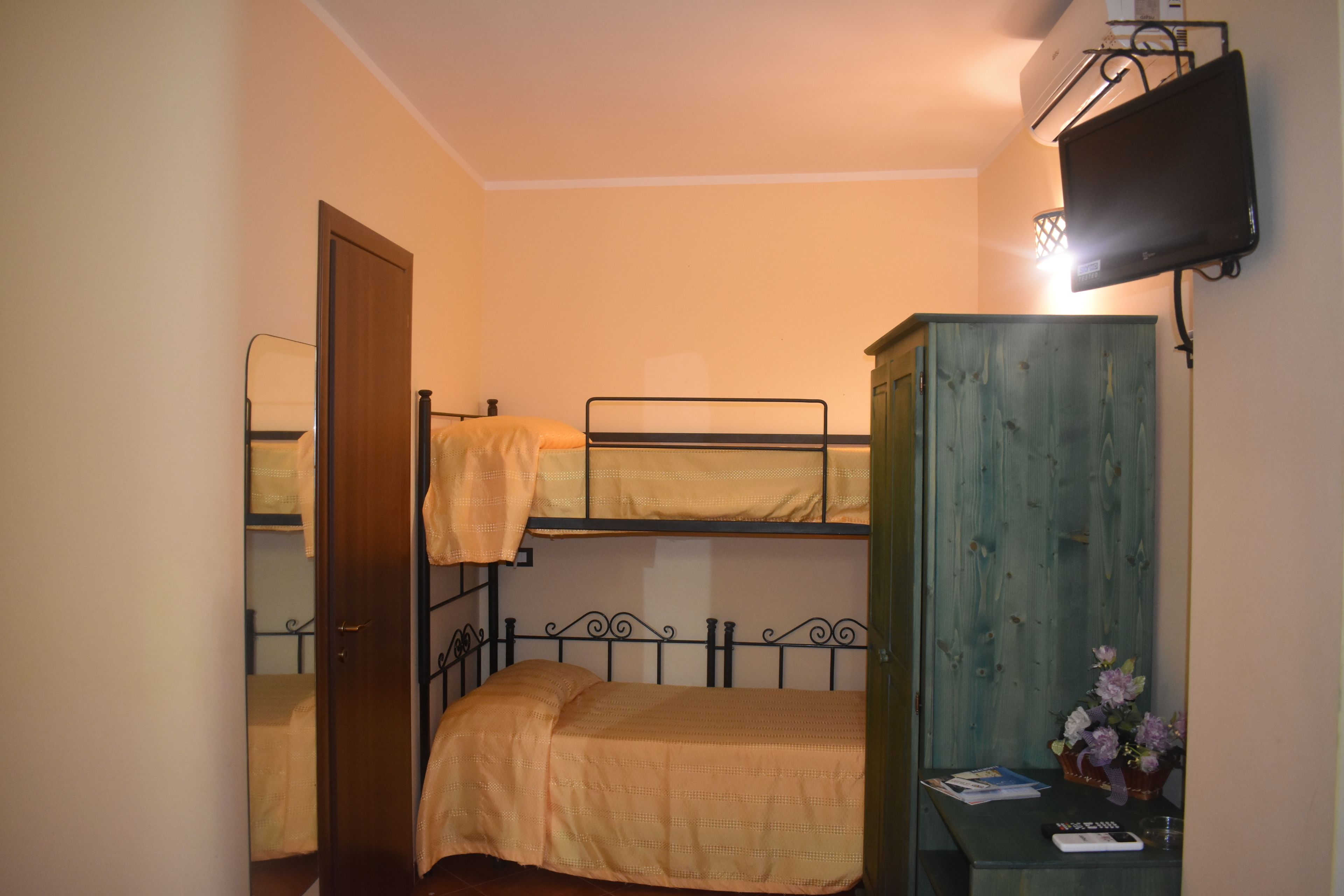 Une chambre de dortoir avec des lits superposés, une armoire en bois, un téléviseur et une petite table sur laquelle est posé un vase de fleurs.