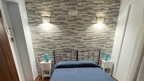 A bedroom with a bed, two bedside tables, a wall-mounted light fixture, and a door.