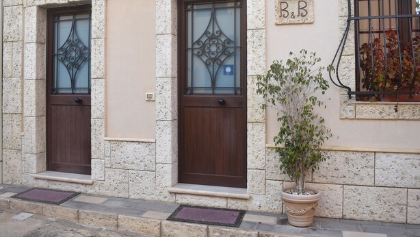 A building with two wooden doors, a potted plant, and a window with a metal grill.