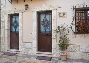 Un edificio con dos puertas de madera, una planta en maceta y una ventana con reja de metal.