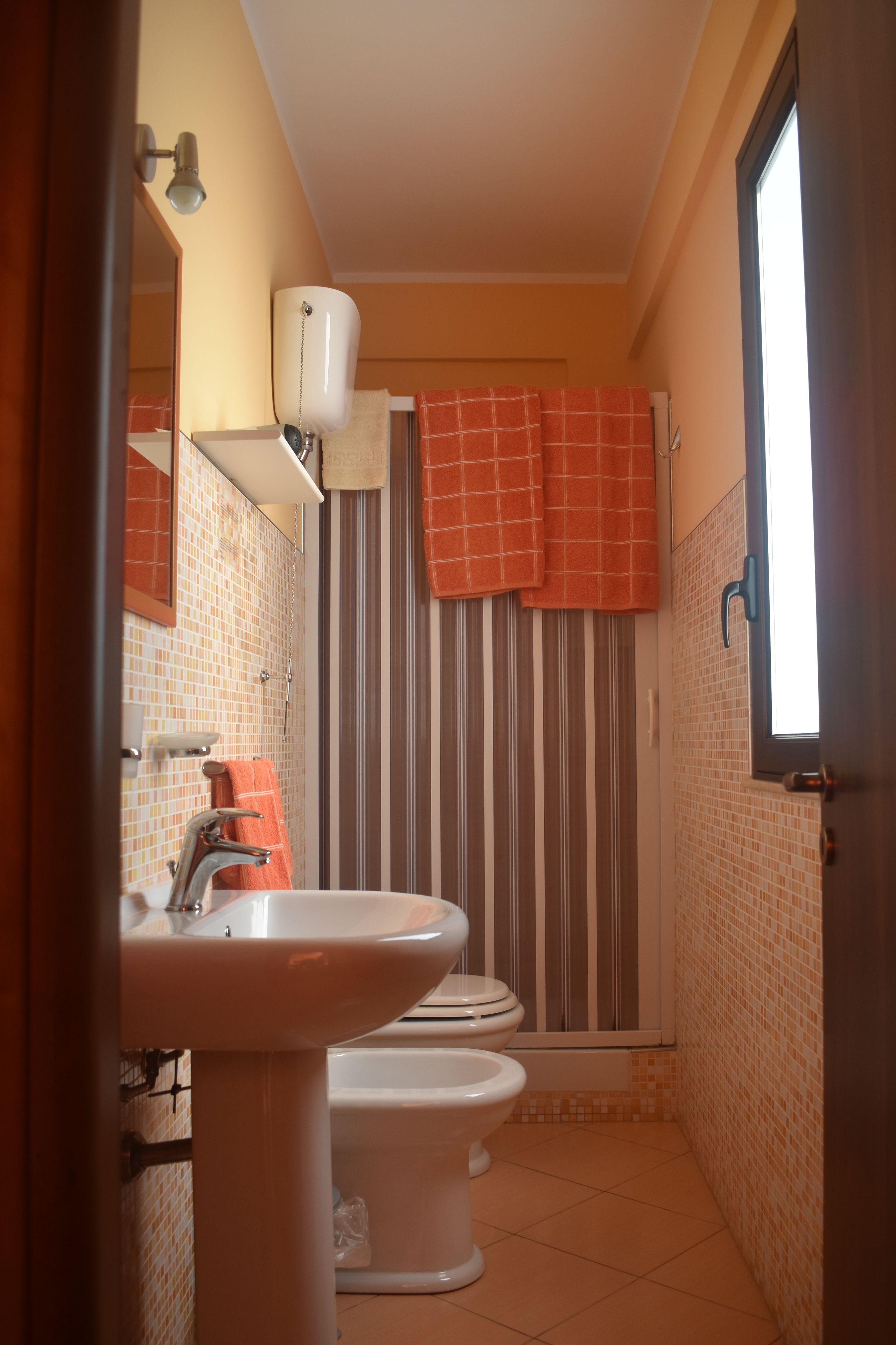 A bathroom with two toilets, a sink, a shower, and striped curtains.