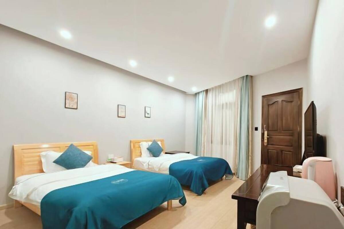 A hotel room with two beds, a desk, a chair, and a television.