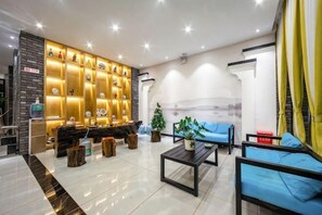 A modern hotel lobby with a reception desk, seating area, and a decorative wall. - Hongsen Business Hotel (Tengchong)