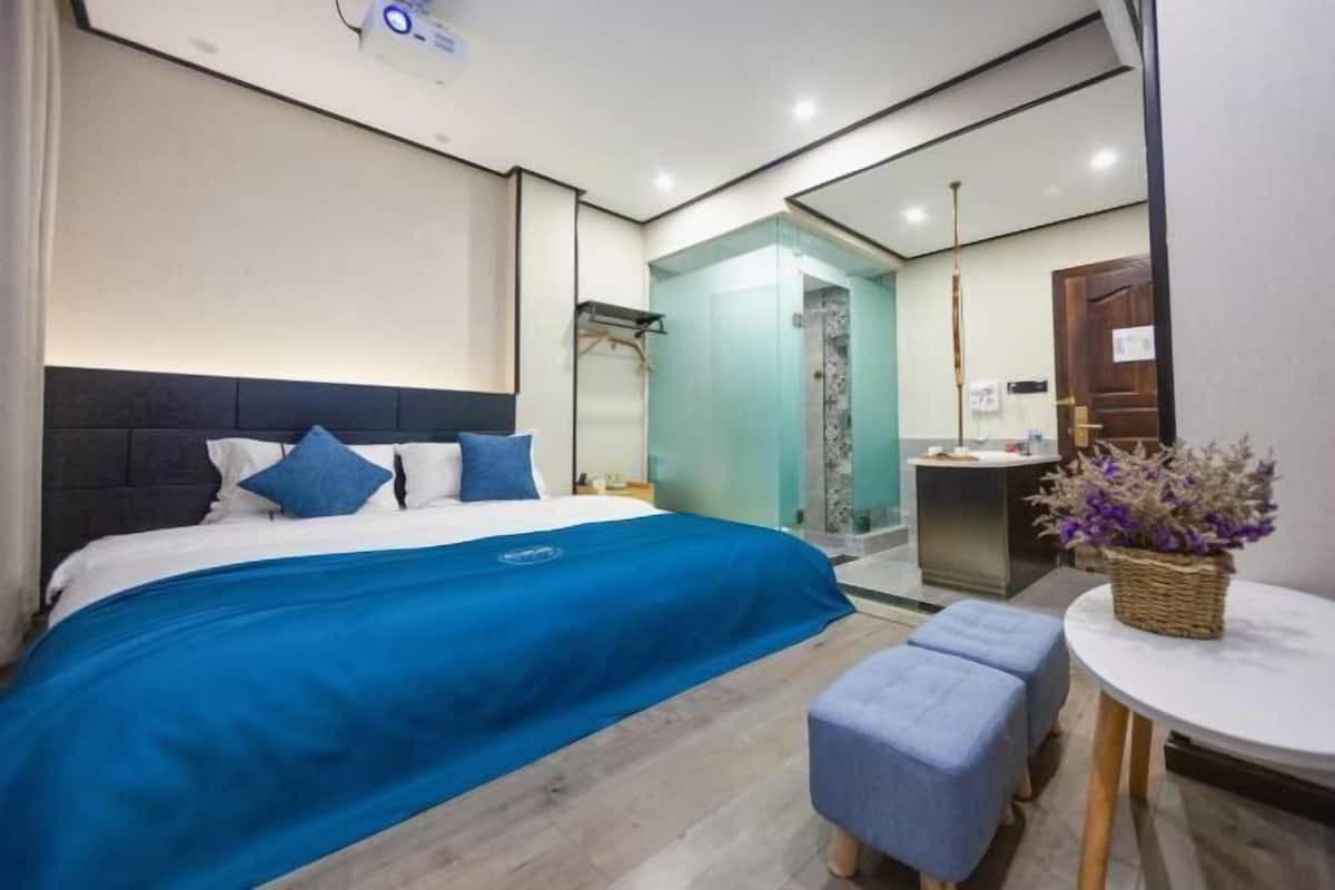 A modern hotel room with a large bed, a small table, and a shower area.