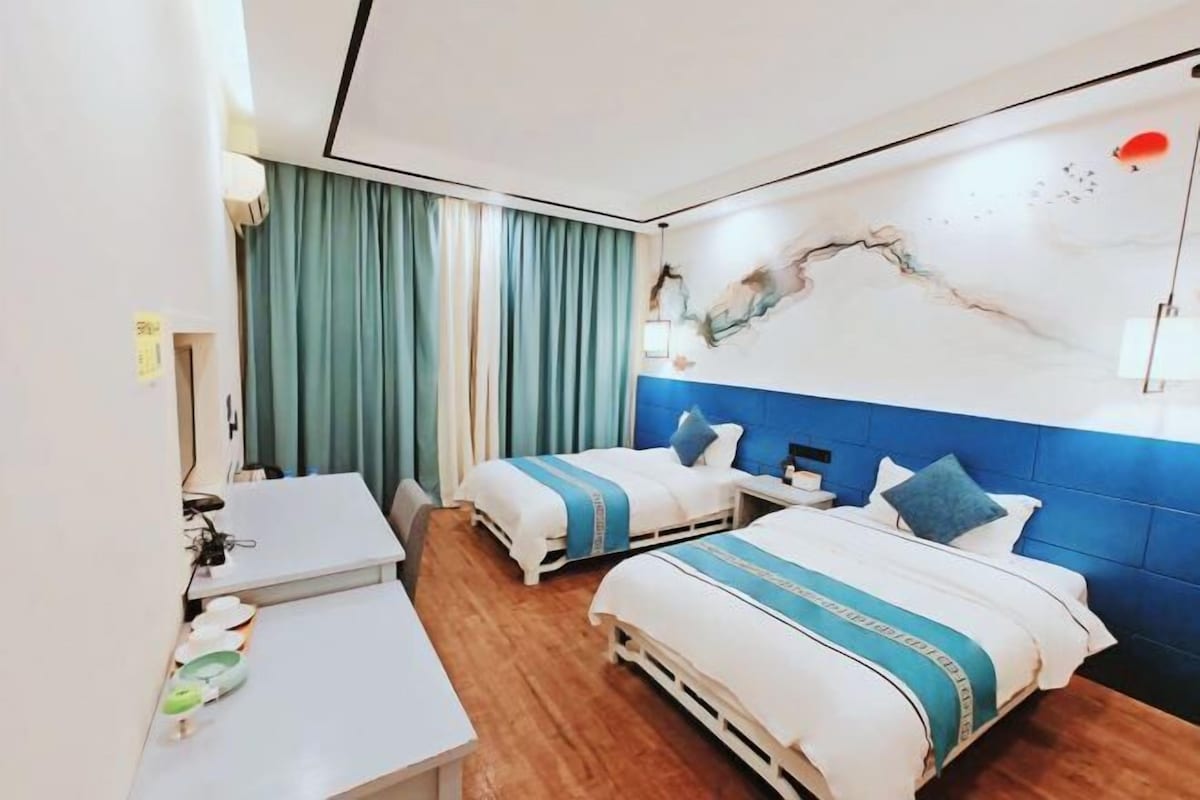 A hotel room with two beds, a desk, and a large abstract painting on the wall.