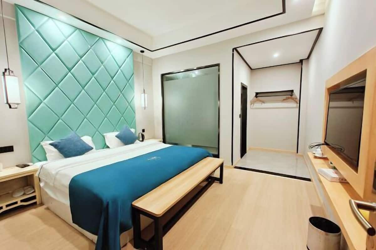 A modern hotel room with a bed, bench, wardrobe, and a television.