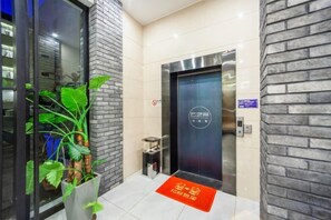 A modern elevator with a logo, a potted plant, and a red mat in a lobby area. - Hongsen Business Hotel (Tengchong)