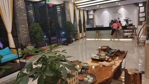 A modern hotel lobby with a reception desk, seating area, and a large plant in the foreground. - Hongsen Business Hotel (Tengchong)