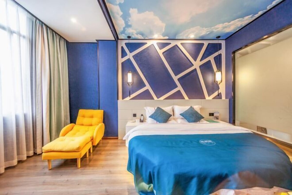 A hotel room with a bed, a yellow armchair, a wall with geometric patterns, and a ceiling with a cloud design.