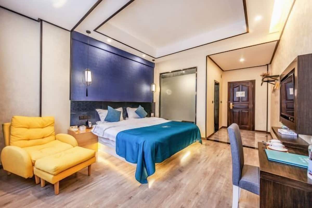 A modern hotel room with a bed, a yellow armchair, a desk, and a wardrobe.