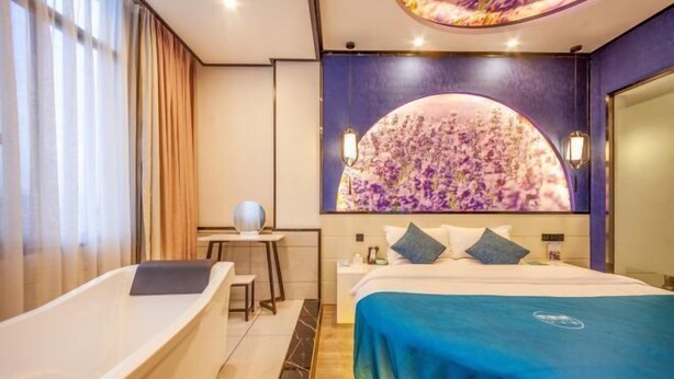A hotel room with a large bed, a bathtub, a desk, and a wall-mounted artwork. - Hongsen Business Hotel (Tengchong)