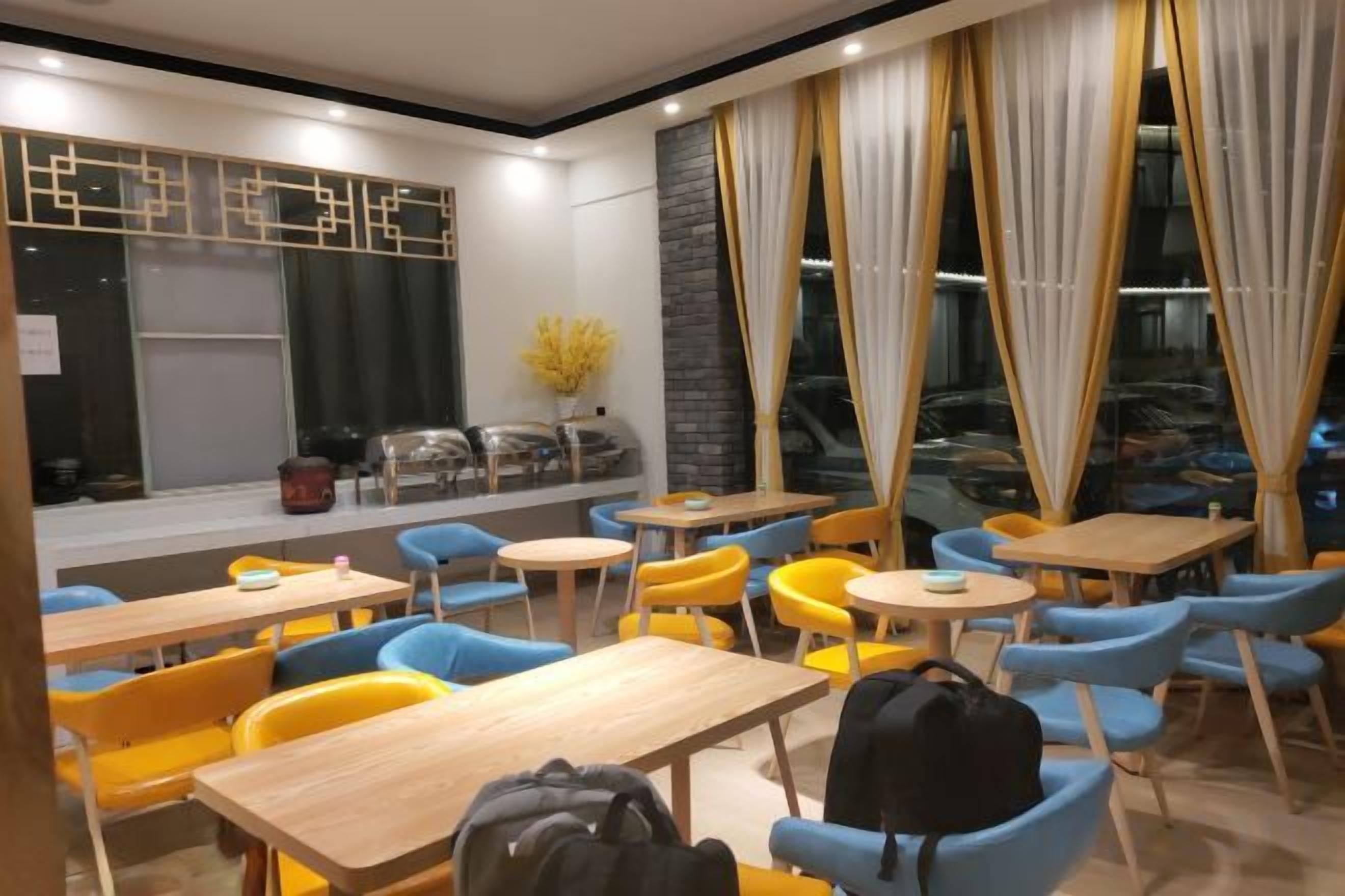 Un comedor moderno con mesas y sillas, un ventanal con cortinas y un muro decorativo.