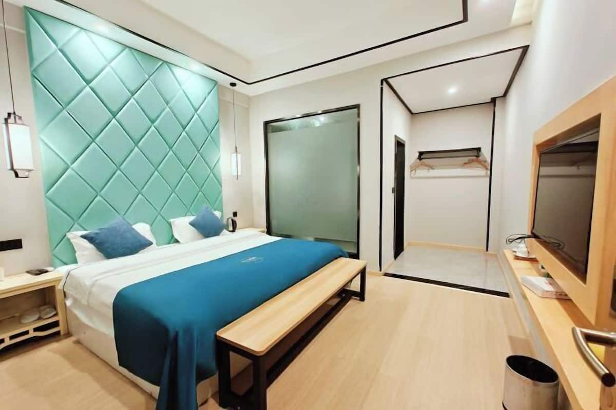 A modern hotel room with a bed, a bench, a TV, and a wardrobe.