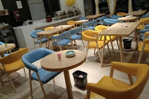 A dining area with round tables and chairs, a trash bin, and a counter with a coffee machine. - Hongsen Business Hotel (Tengchong)