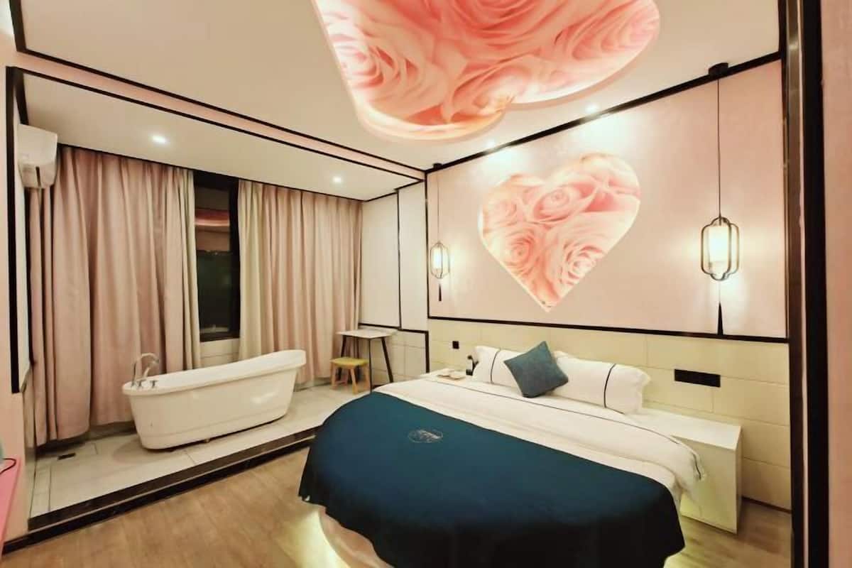 A modern hotel room with a large bed, a bathtub, and a wall with a heart-shaped design.