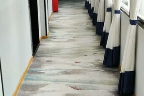 A corridor with a patterned floor, a row of umbrellas on the right, and a door on the left. - Hongsen Business Hotel (Tengchong)