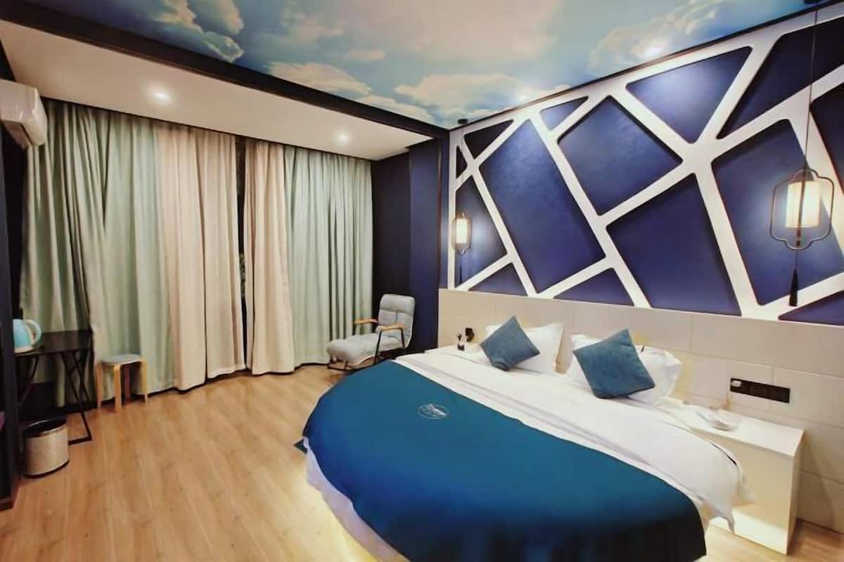 A modern hotel room with a large bed, a headboard with geometric patterns, a ceiling mural, and a nightstand.