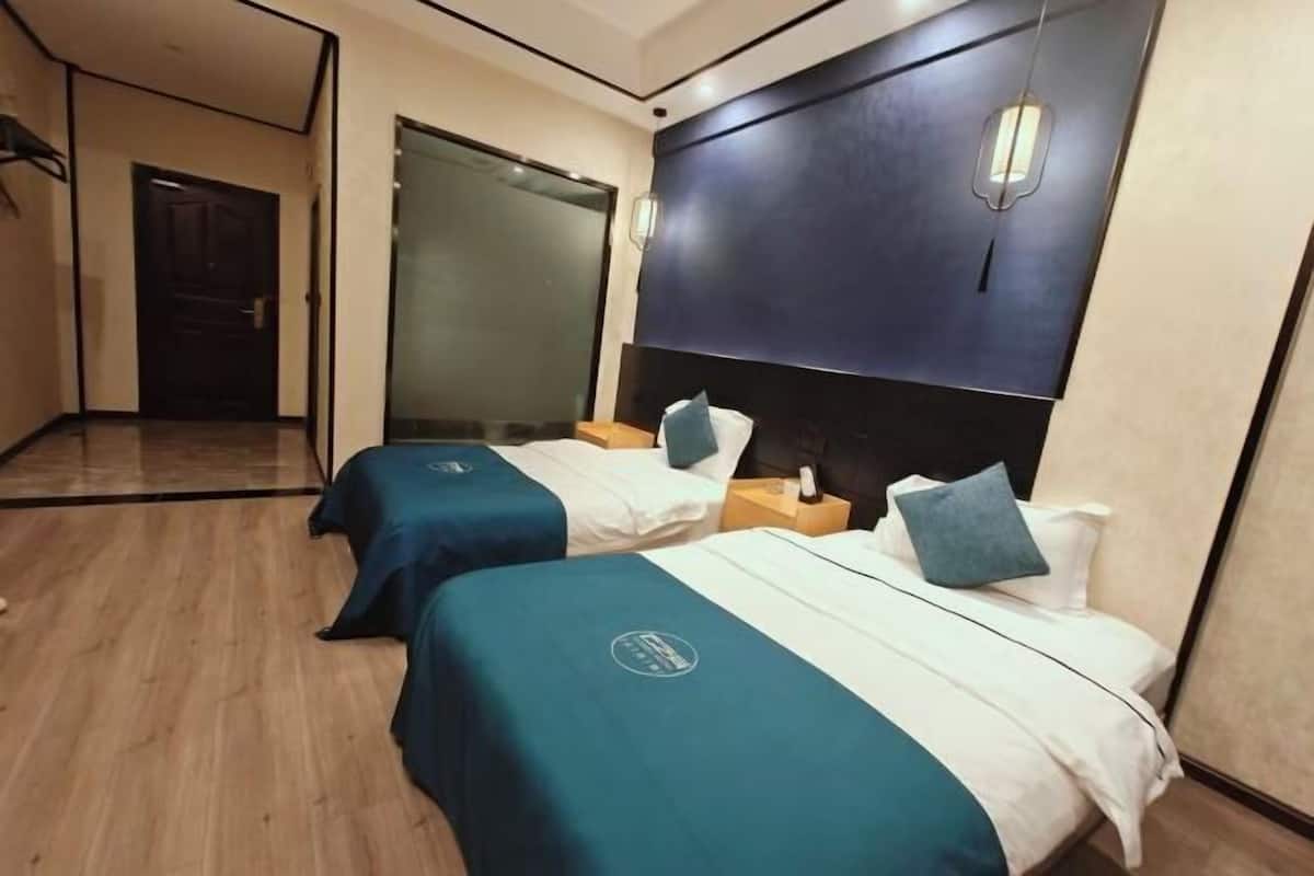A hotel room with two beds, a dark headboard, a wooden floor, and a glass door leading to another room.