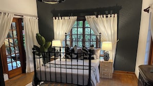 Ein Schlafzimmer mit Himmelbett, zwei Nachttischen mit Lampen, einer Holzkiste und Blick durch das Fenster.