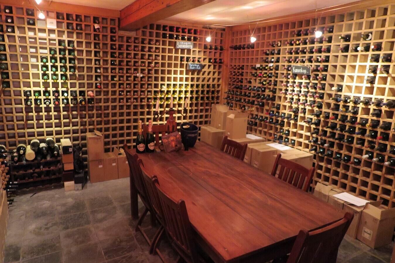 Una bodega con estanterías de madera llenas de botellas, una larga mesa de madera y sillas.