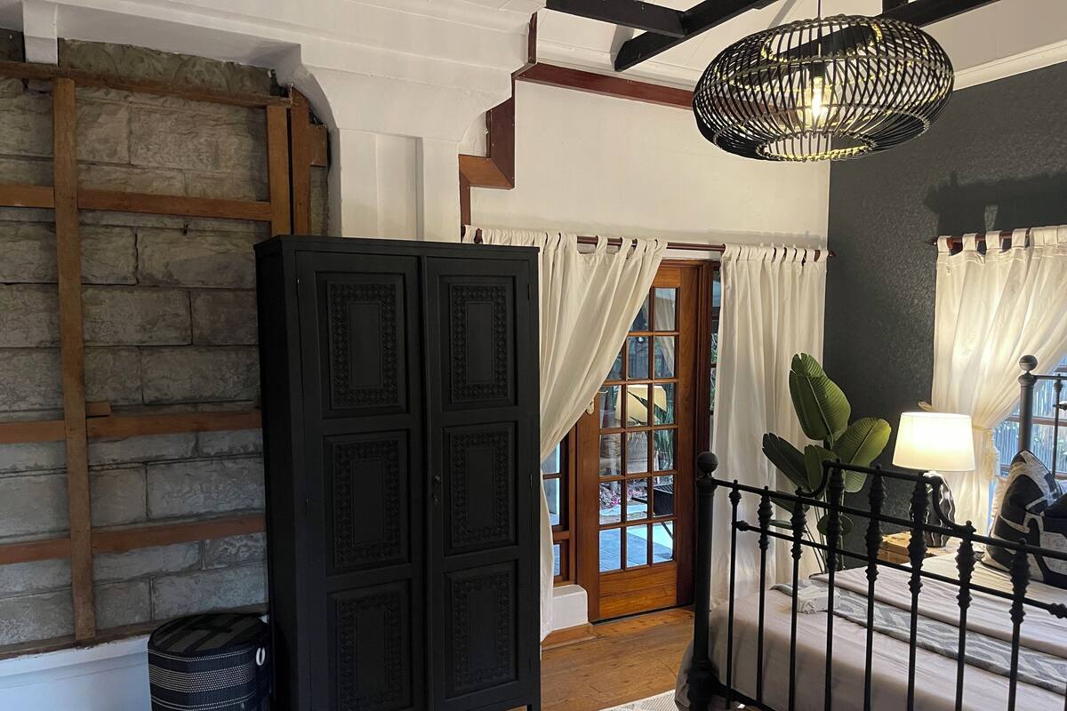 A room with a black cabinet, a staircase, a bed with a black metal frame, and a hanging light fixture.