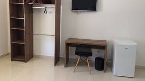 Quarto com guarda-roupa de madeira, escrivaninha com cadeira, televisão e mini-frigorífico branco.