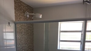 Casa de banho com chuveiro separado por vidro, sanita e janela que permite entrada de luz natural.