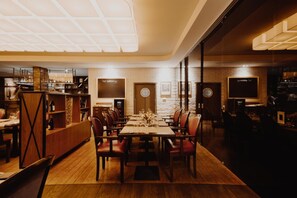 A restaurant with a long dining table, multiple chairs, a bar area, and a brick wall.