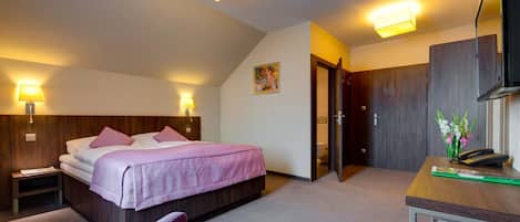 A hotel room with a bed, bedside lamps, a desk, a chair, and a television.