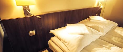 A hotel room with a bed, a nightstand, and a wall-mounted lamp.
