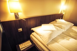 A hotel room with a bed, a nightstand, and a wall-mounted lamp.