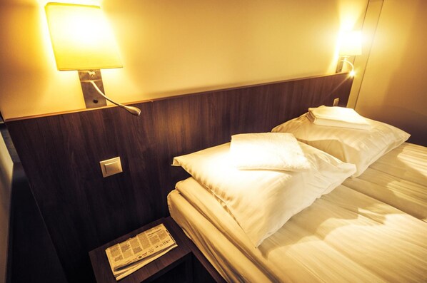 Una habitación de hotel con una cama, una mesita de noche y una lámpara de pared.