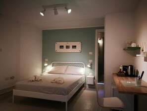 Quarto com cama, luminárias de cabeceira, escrivaninha e cadeira.