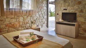 A stone-walled room with a TV, a wicker basket with toiletries, and a view of the outdoors. - Nefeli Luxury Villas (Kassandra)