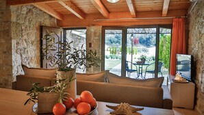 A cozy room with a wooden ceiling, stone walls, a sofa, a table with oranges and a plant, and a TV on a side table. - Nefeli Luxury Villas (Kassandra)