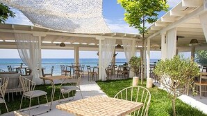 An outdoor dining area with tables and chairs, a grassy area, and a view of the sea. - Nefeli Luxury Villas (Kassandra)