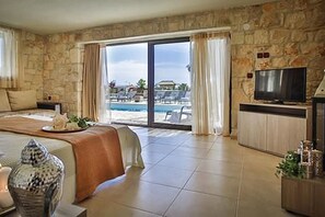 A hotel room with a stone wall, a bed with a view of a pool, a TV, and a dining area.