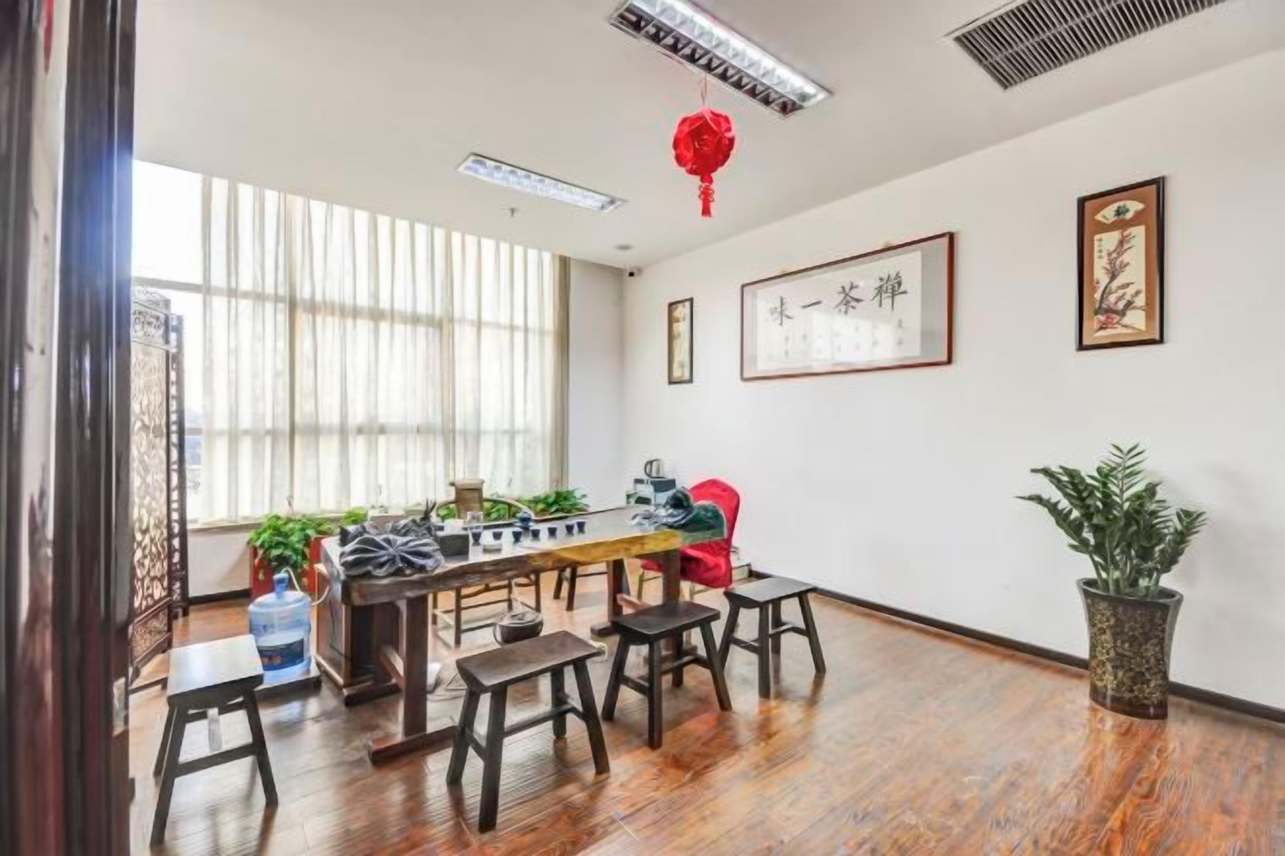 A room with a wooden floor, a table with chairs, a large window, and a red hanging ornament.