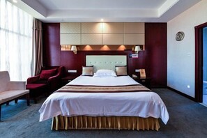 Habitación de hotel con una cama grande, un escritorio, una silla y un ventanal con cortinas.