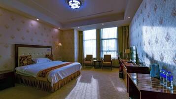Habitación de hotel con una cama grande, un escritorio con silla, televisión y ventana con cortinas.