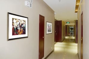 Un couloir aux murs ornés de tableaux encadrés, avec des portes et un plancher ciré.