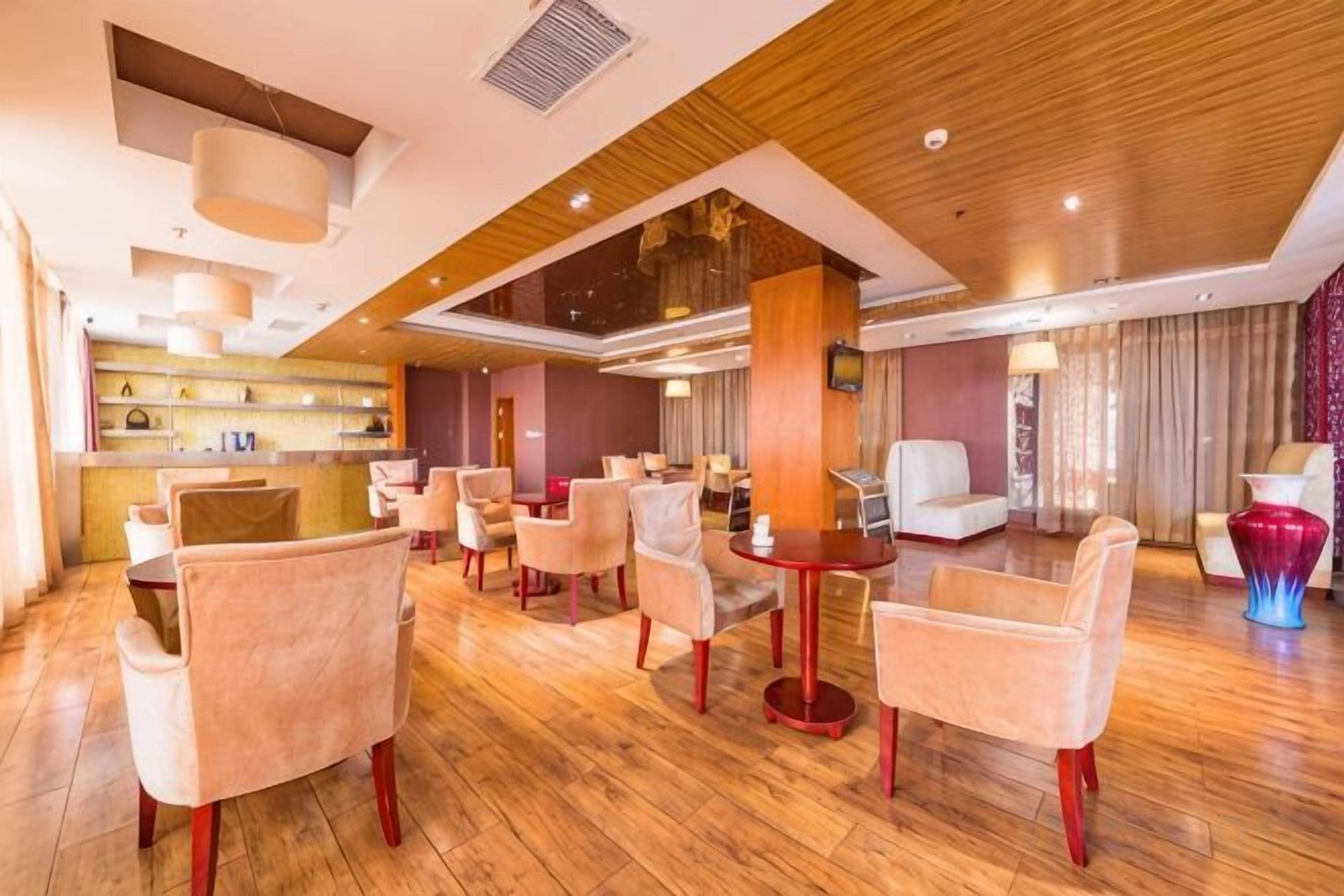 A hotel lobby with a wooden floor, multiple seating areas, and a reception desk.