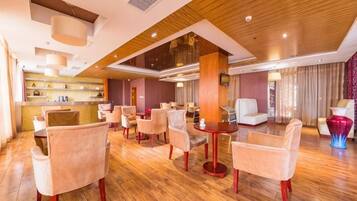 A hotel lobby with a wooden floor, multiple seating areas, and a reception desk.