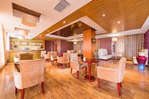 A hotel lobby with a wooden floor, multiple seating areas, and a reception desk.